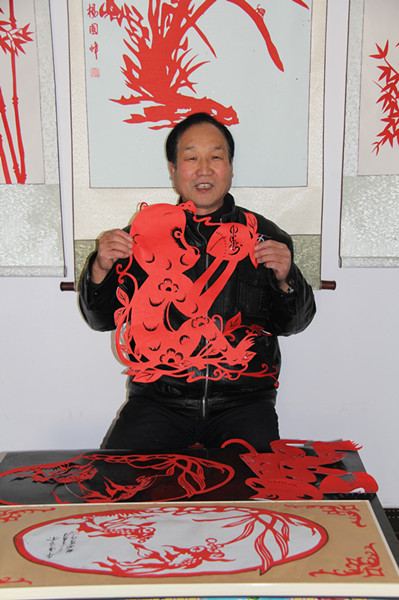 杨国峰正在展示刚刚剪出的金猴献寿的剪纸作品