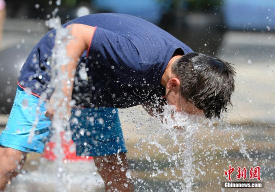 一名小孩将头伸向北京街头的喷泉以降温祛暑