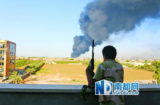 2日，利比亚首都的黎波里，一民兵武装成员眺望被火箭弹击中的储油罐冒出浓烟。