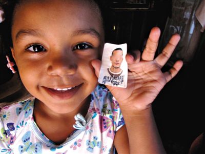 5岁的海地女孩萨沙·巴里奥斯拿着一张照片。母亲罗莎莱恩·杜佩瓦勒告诉她，这是她的父亲，一名来自乌拉圭的维和人员。
