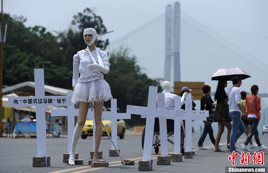 4月16日，重庆市洋人街上,受伤的塑料人像“模特”旁打出标语向“中国式过马路”说不，告诫市民要遵守