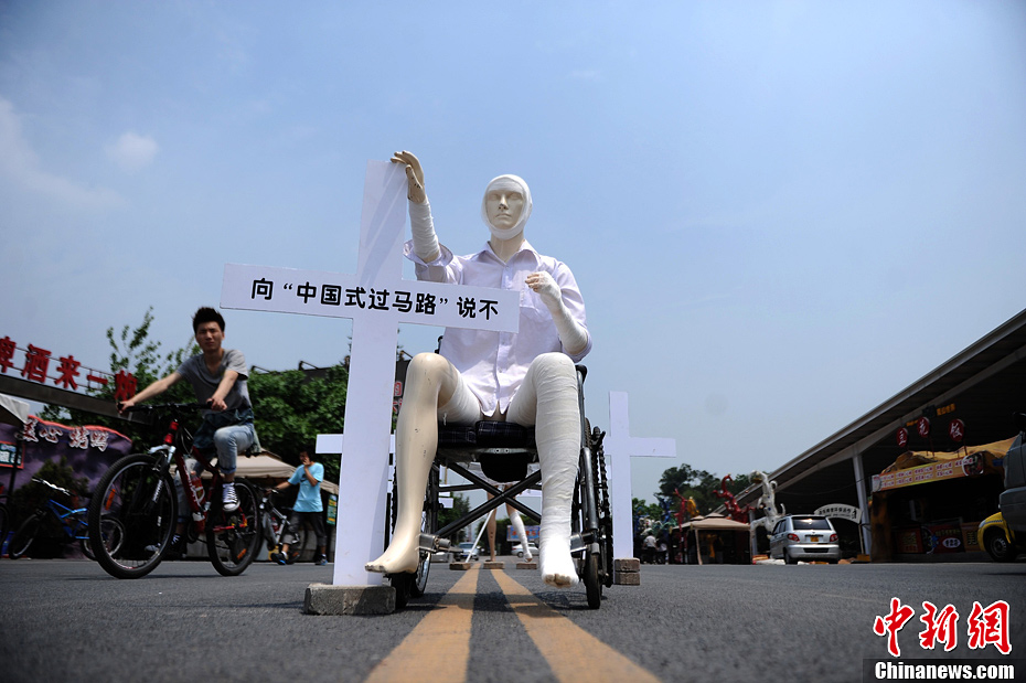 4月16日，重庆市洋人街上摆放着两个受了伤的塑料人像“模特”，旁边十字架上写着向“中国式过马路”说不