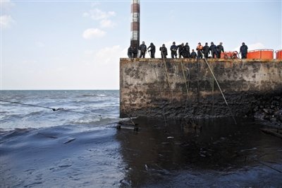 昨日，山东青岛，清污人员正在海边清理油污。