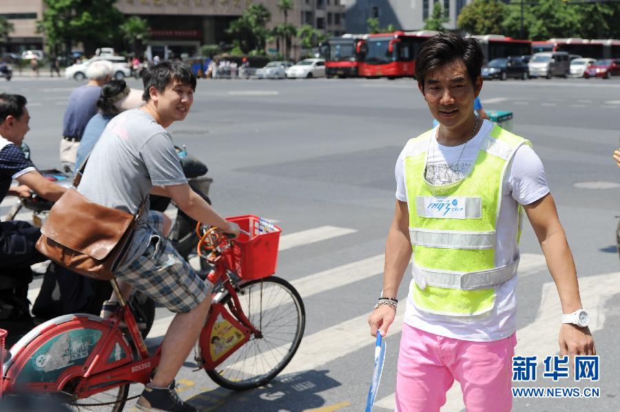 6月17日，任贤齐（右）手拿指示牌在杭州街头做交通协管员，劝导行人遵守交通规则。