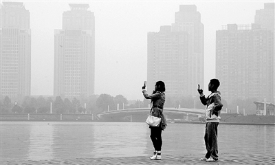 29日中午，郑东新区如意湖畔，两个年轻人拍摄雾霾中的景色。 郑州晚报记者 马健 图