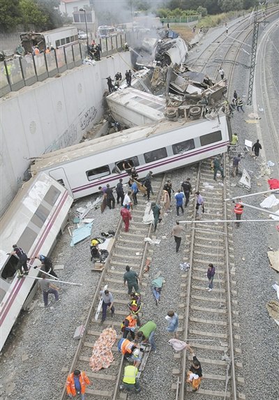 24日，救援人员在西班牙列车脱轨现场。一节车厢被强大的惯性抛上铁道边的高台。