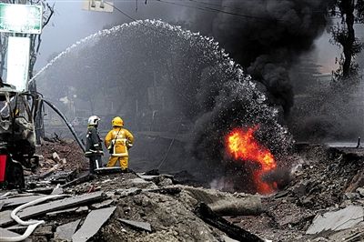 爆炸导致路面被掀翻，多处起火，消防员正在灭火。
