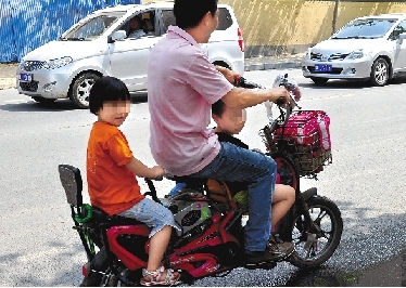 周先生骑着一辆低矮的电动车带着一对儿女，很不安全。