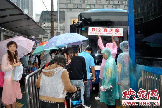 公交志愿者雨中高举“B12-直达车”指示牌疏导返校学生乘车