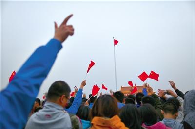 国旗升至旗杆顶部，迎风飘扬。广场上的人们向着国旗挥手。