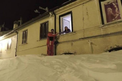 一个居民站在积雪上，可以与一名二楼邻居在窗口握手。（来源：意大利气象局）