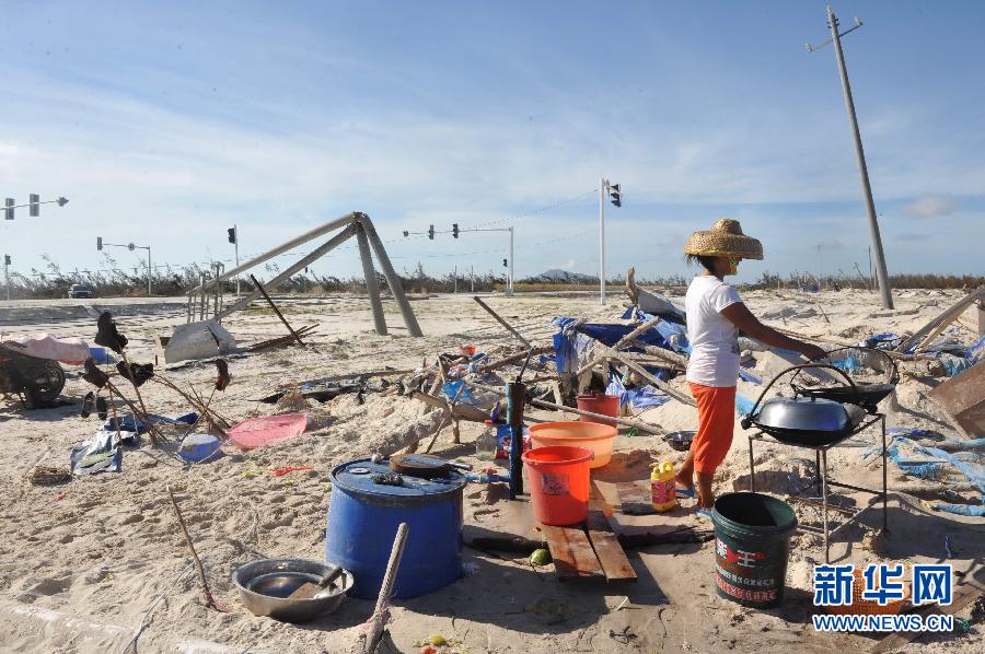 7月22日，海南省文昌市昌洒镇一名居民在风沙掩埋的工棚前做饭。