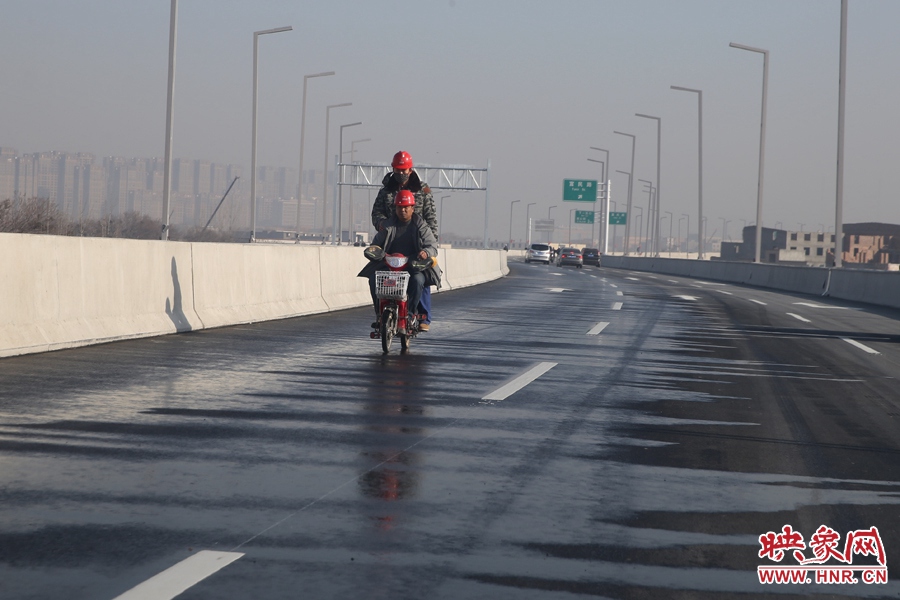 两名工人骑车经过洒水养护路面。