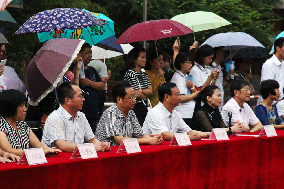 在主席台上观看的校领导也坚持不打伞陪学生一起淋雨，身旁站满了打伞观看的家长。