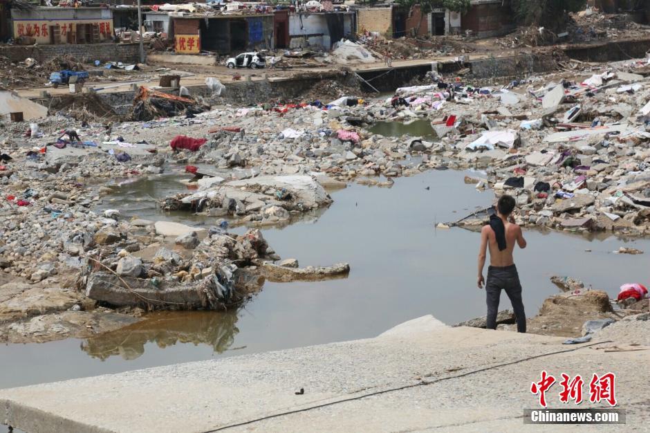 图为一位村民站在洪水退去的河边打电话。