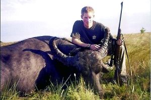 哈里王子手持猎枪，蹲在一头遭到猎杀的水牛旁边