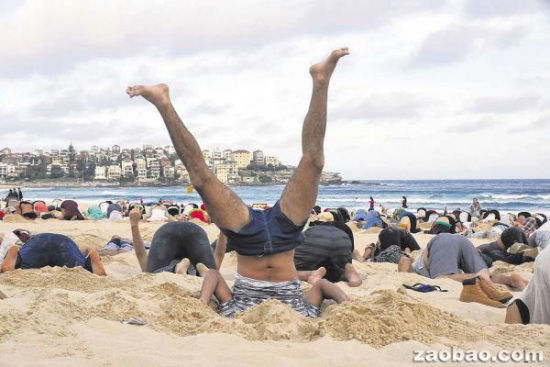 图为澳大利亚人沙滩上挖坑埋头装鸵鸟，抗议澳大利亚政府对气候变化问题无动于衷。
