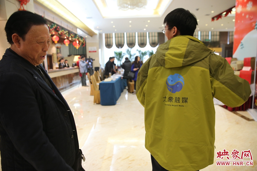 大象融媒映象网记者王宽，向省政协委员张树才展示大象融媒报道两会的统一服装。