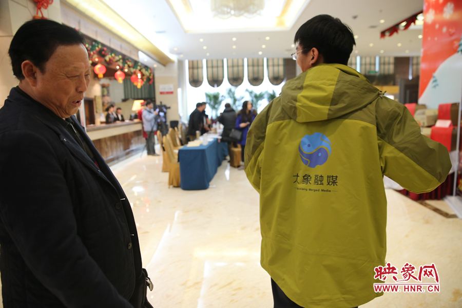 大象融媒映象网记者王宽，向省政协委员张树才展示大象融媒报道两会的统一服装。