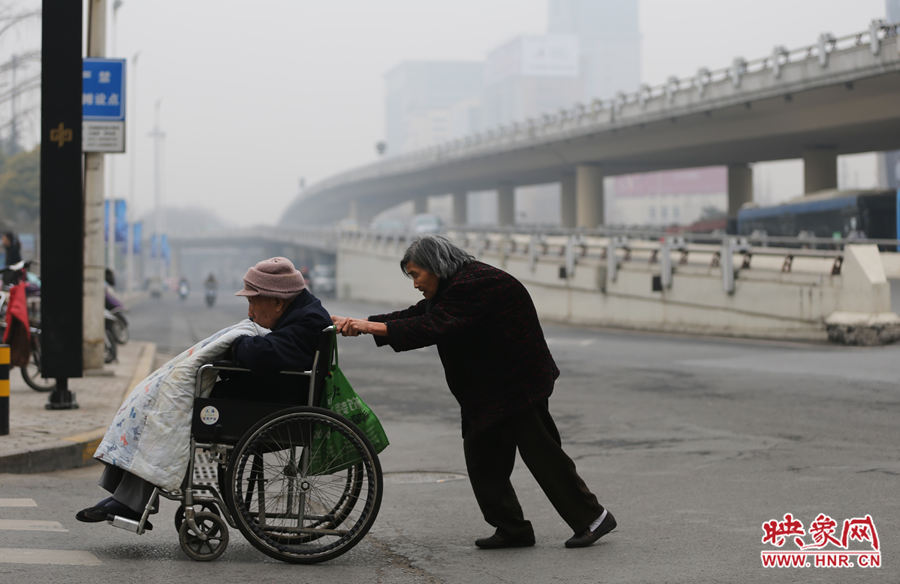 老太太推着轮椅上的老人虽然有些吃力,但车少了,不用再抢着过马路了.